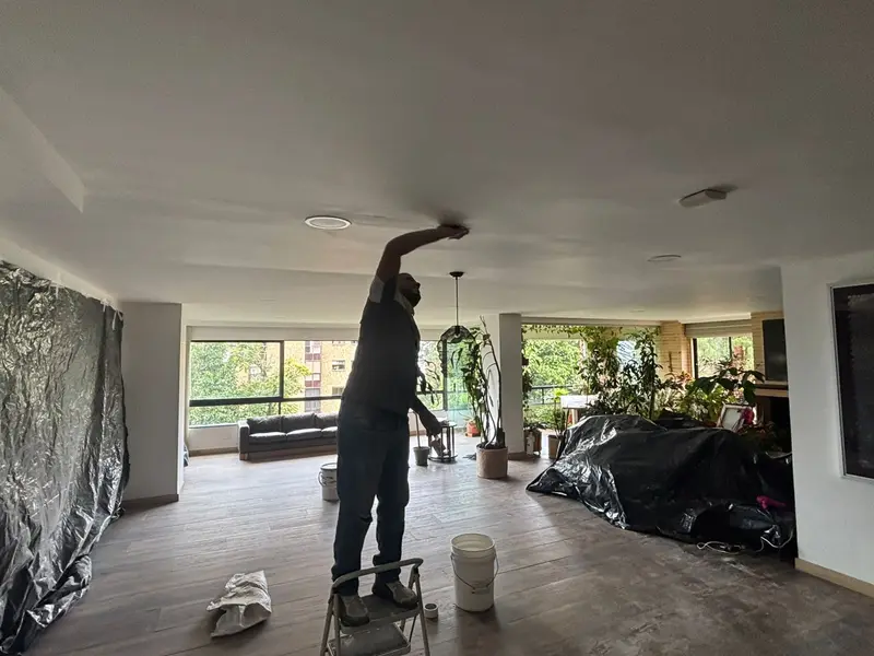 Acabados de pintura en el techo de un apartamento con los muebles protegidos